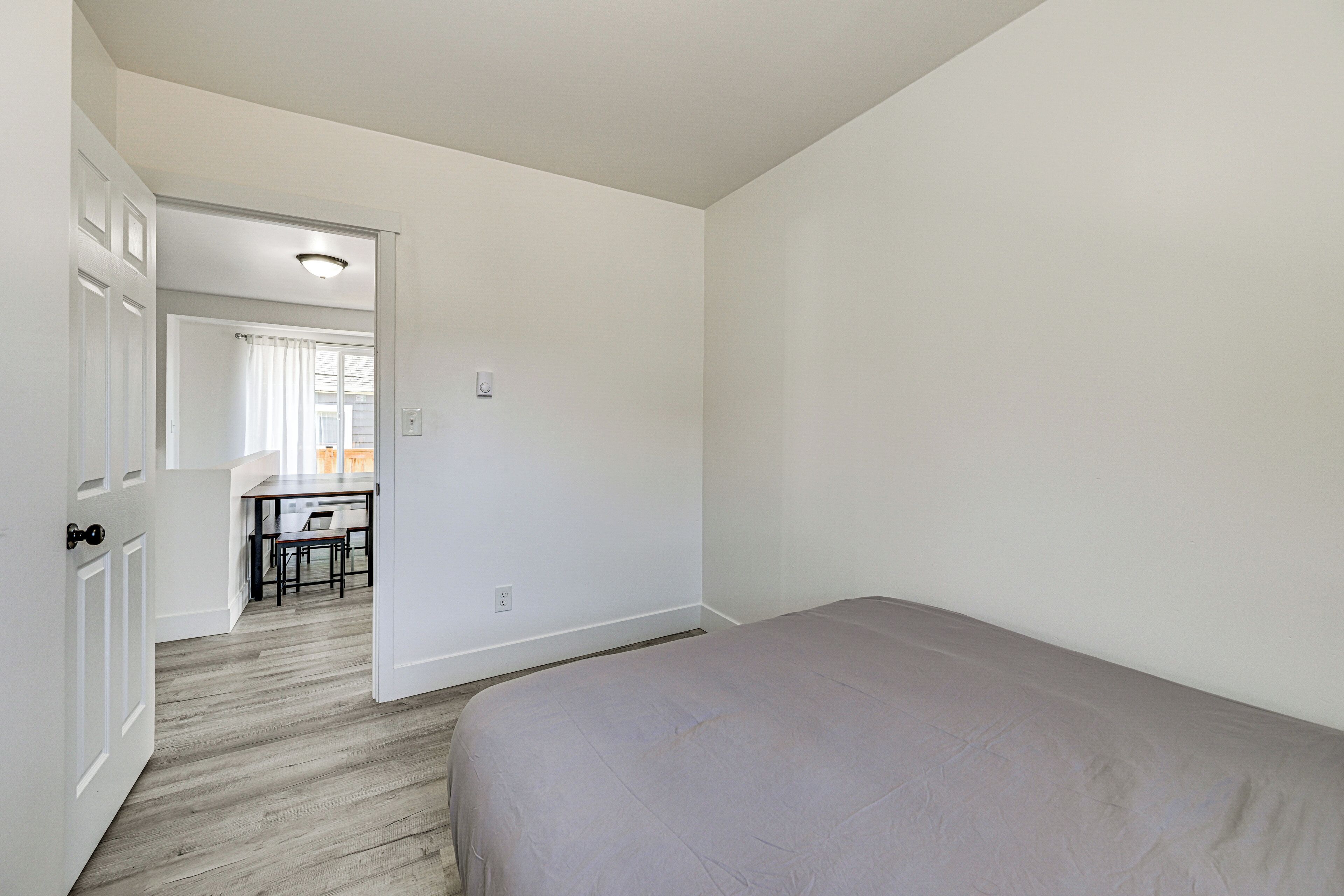 A bedroom with a bed, a door leading to a bathroom, and a view of a dining area.