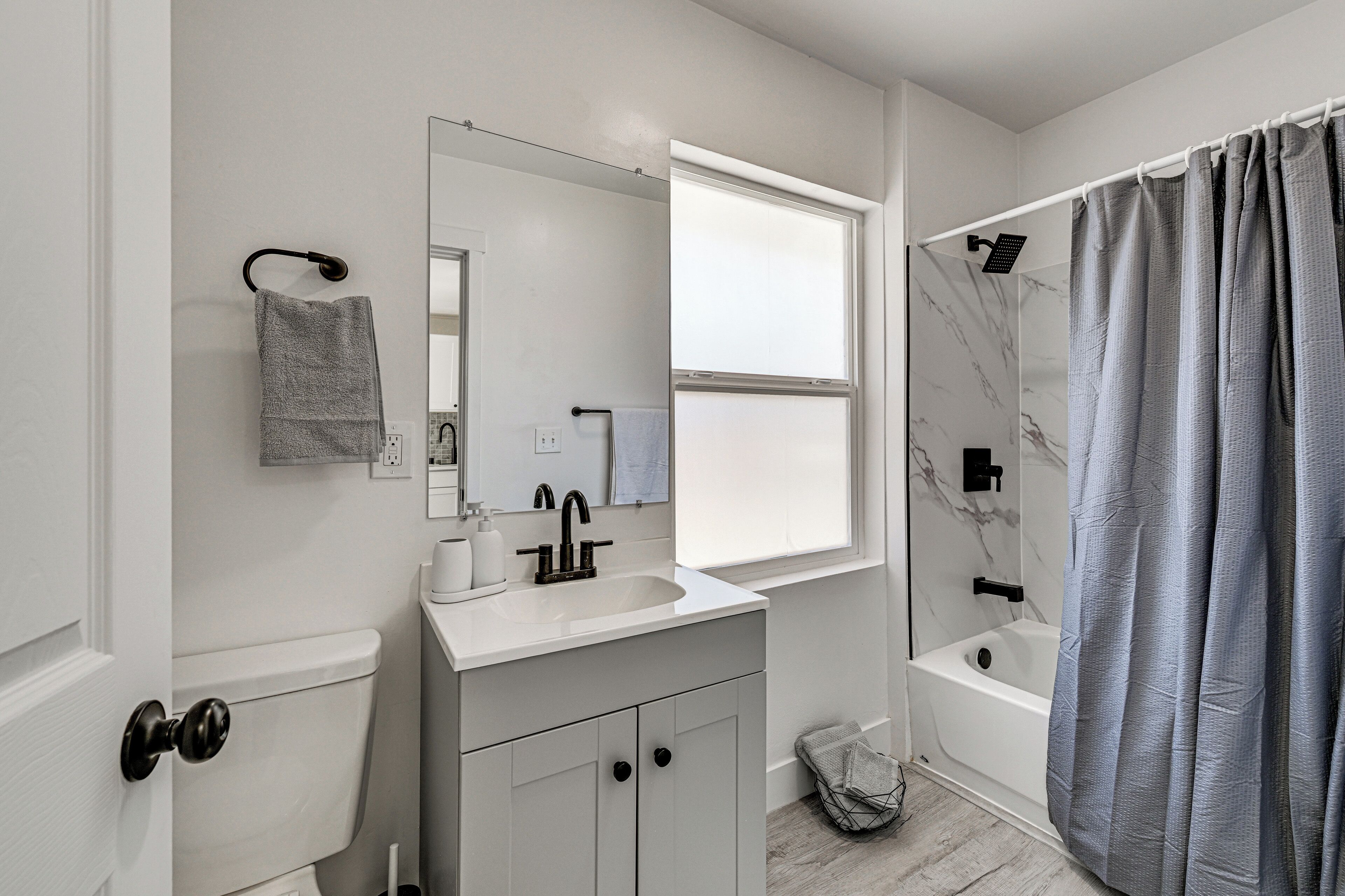 Ein Badezimmer mit Toilette, Waschbecken, Spiegel, Dusche und einem Fenster.