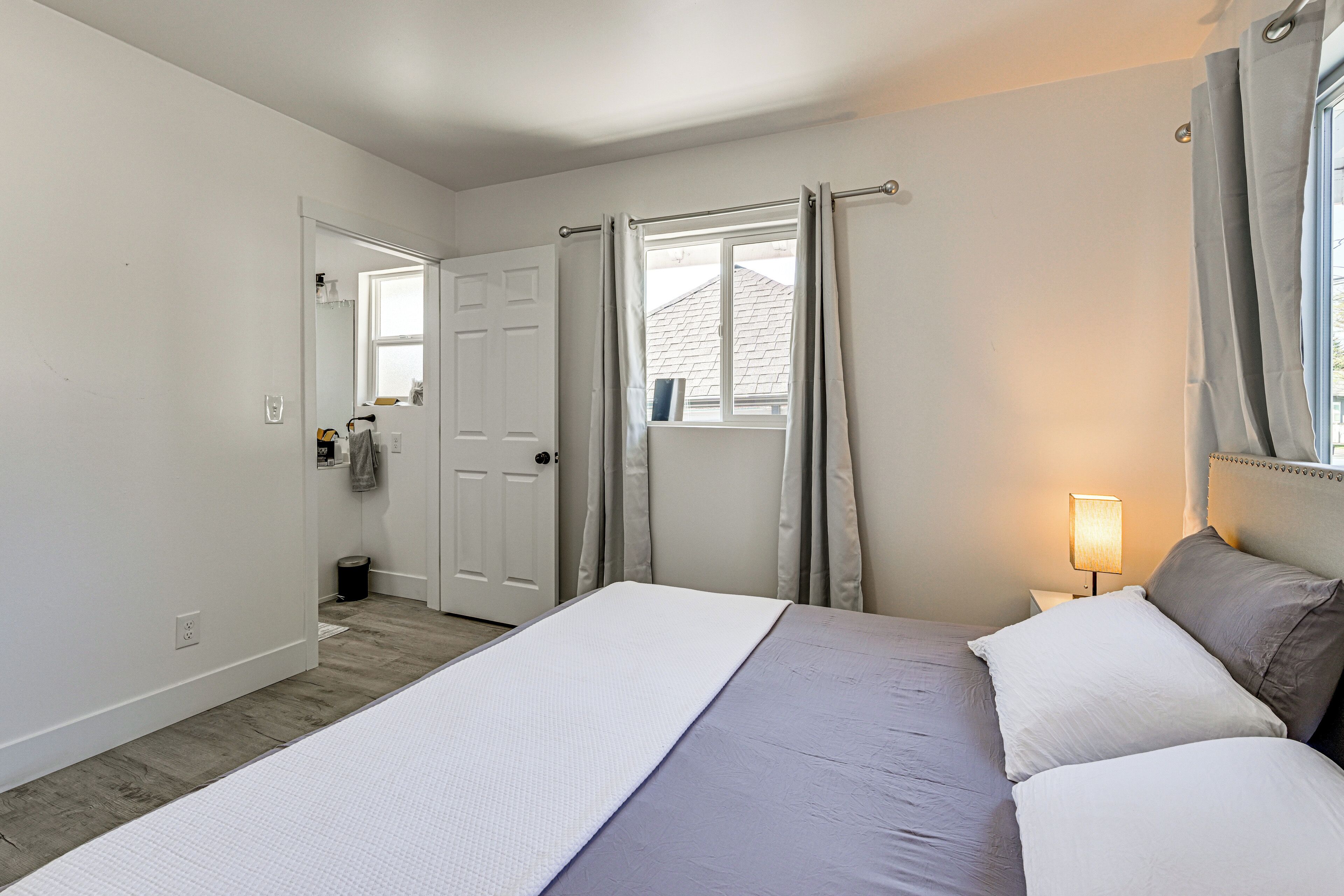 Un dormitorio con cama, cortinas, ventana, mesita de noche y lámpara.