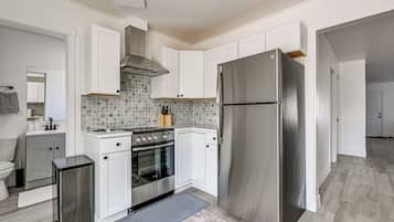 Uma cozinha moderna com armários brancos, geladeira de aço inoxidável, forno embutido e painel de azulejos.