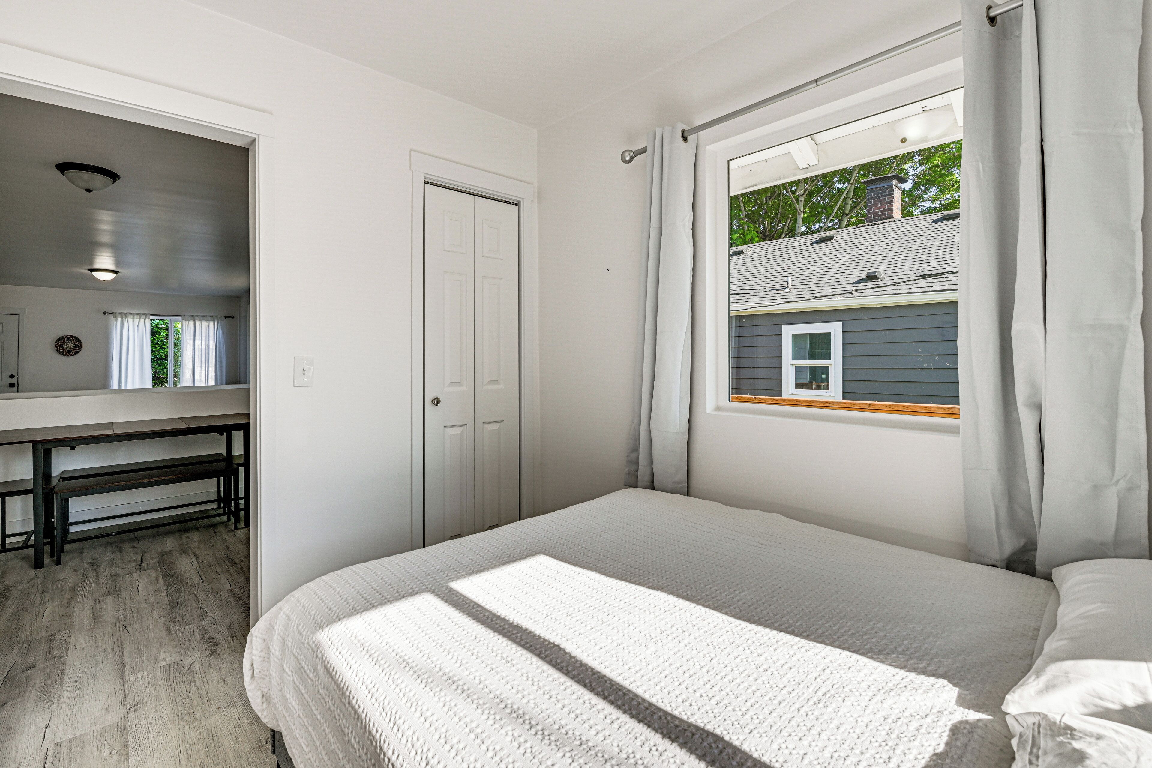 A bedroom with a bed, a window with curtains, a door, and a desk with a bench.
