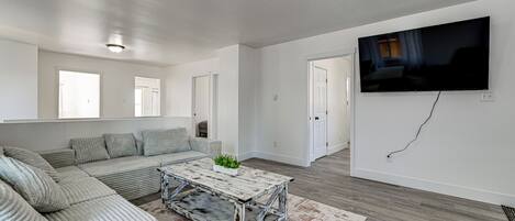 A modern living room with a sectional sofa, a rustic coffee table, a flat-screen TV, and a large window.