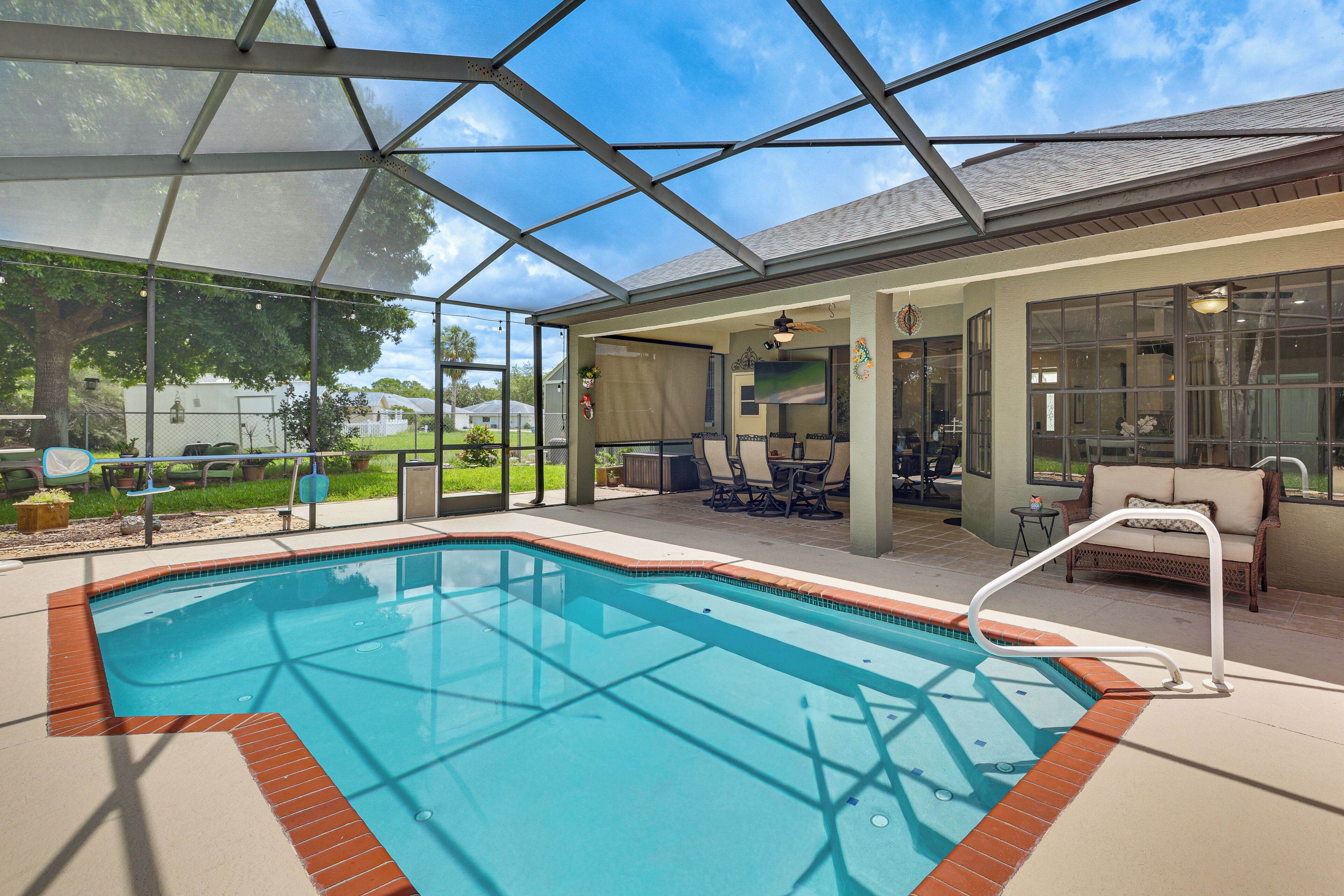 A covered swimming pool with a patio area, chairs, and a view of the outdoors.