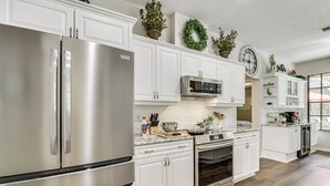 Una cocina moderna con electrodomésticos de acero inoxidable, armarios blancos y plantas decorativas.
