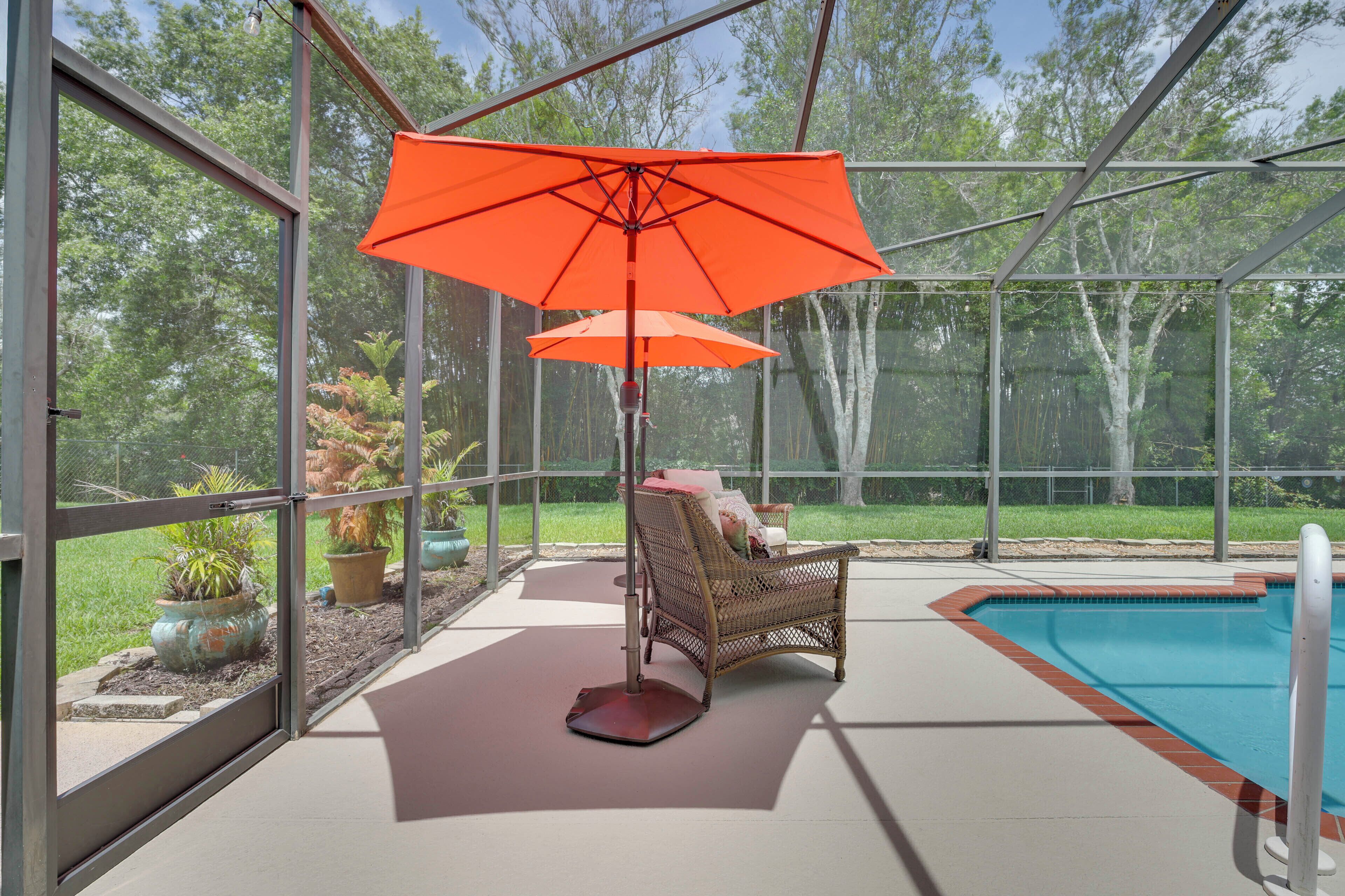 Uma área externa coberta com piscina, uma cadeira de vime e um guarda-sol laranja.