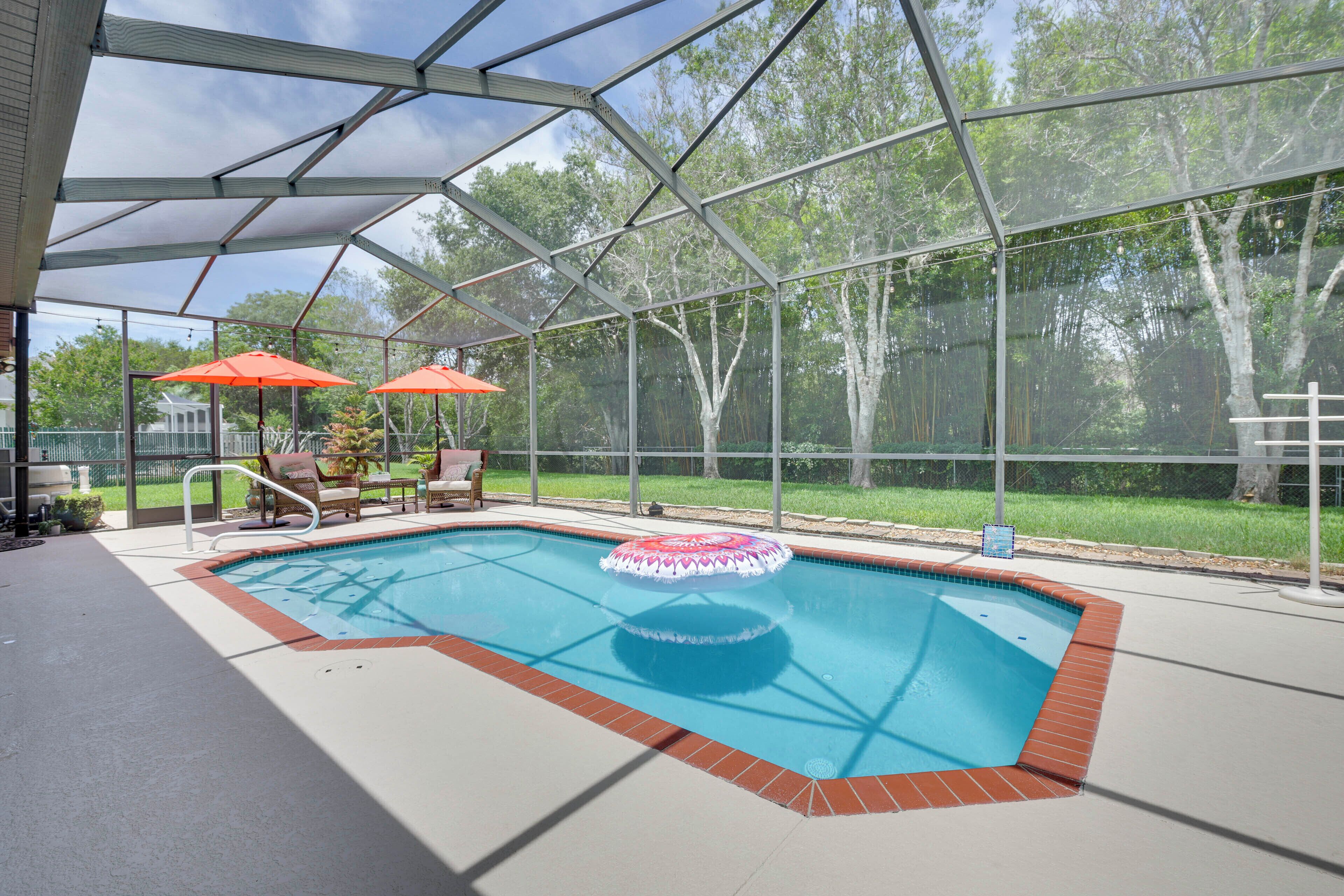 A covered swimming pool with a red border, two red umbrellas, and a poolside chair.