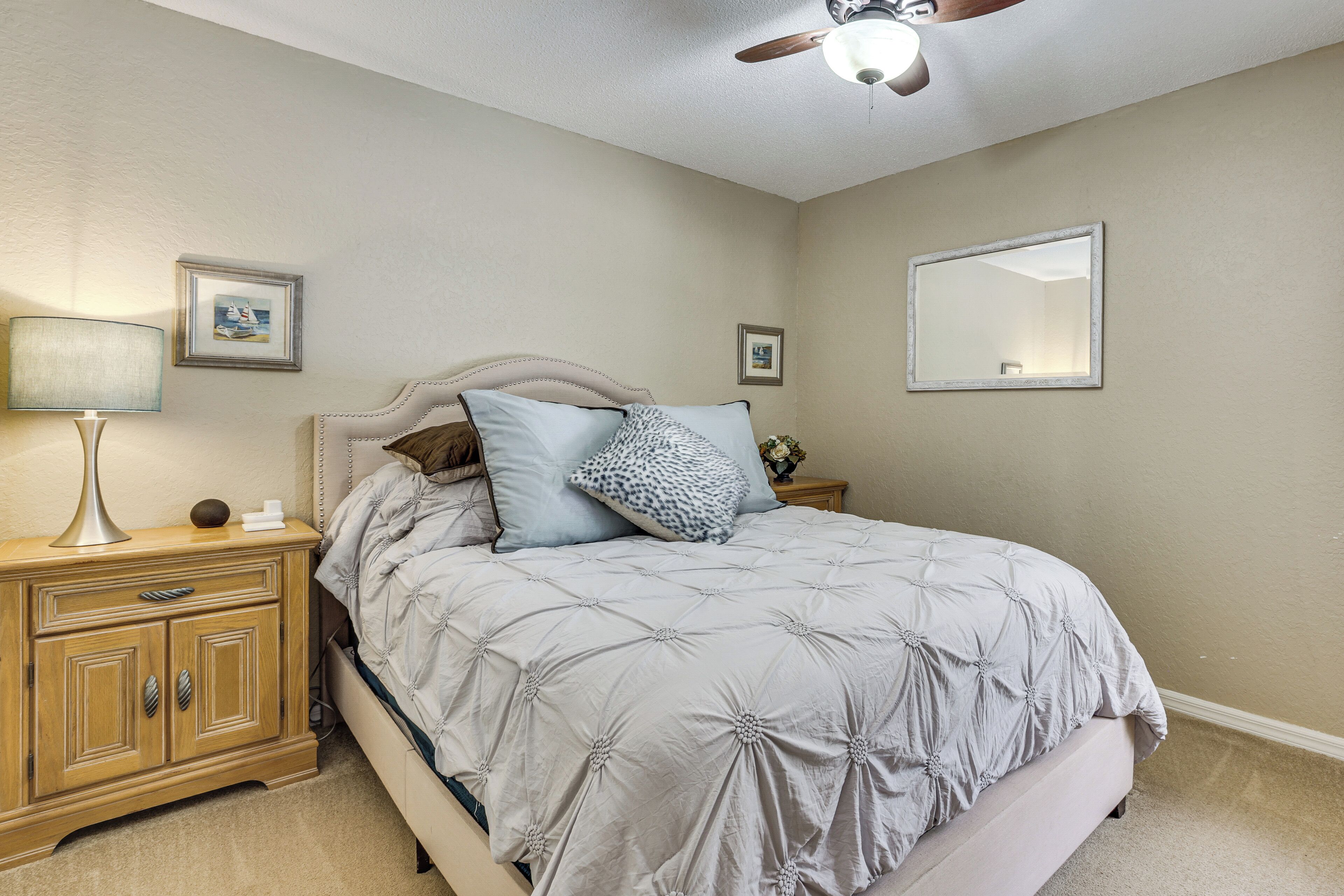 Une chambre à coucher avec un lit, des tables de chevet, une lampe, un ventilateur de plafond et des tableaux encadrés accrochés aux murs.