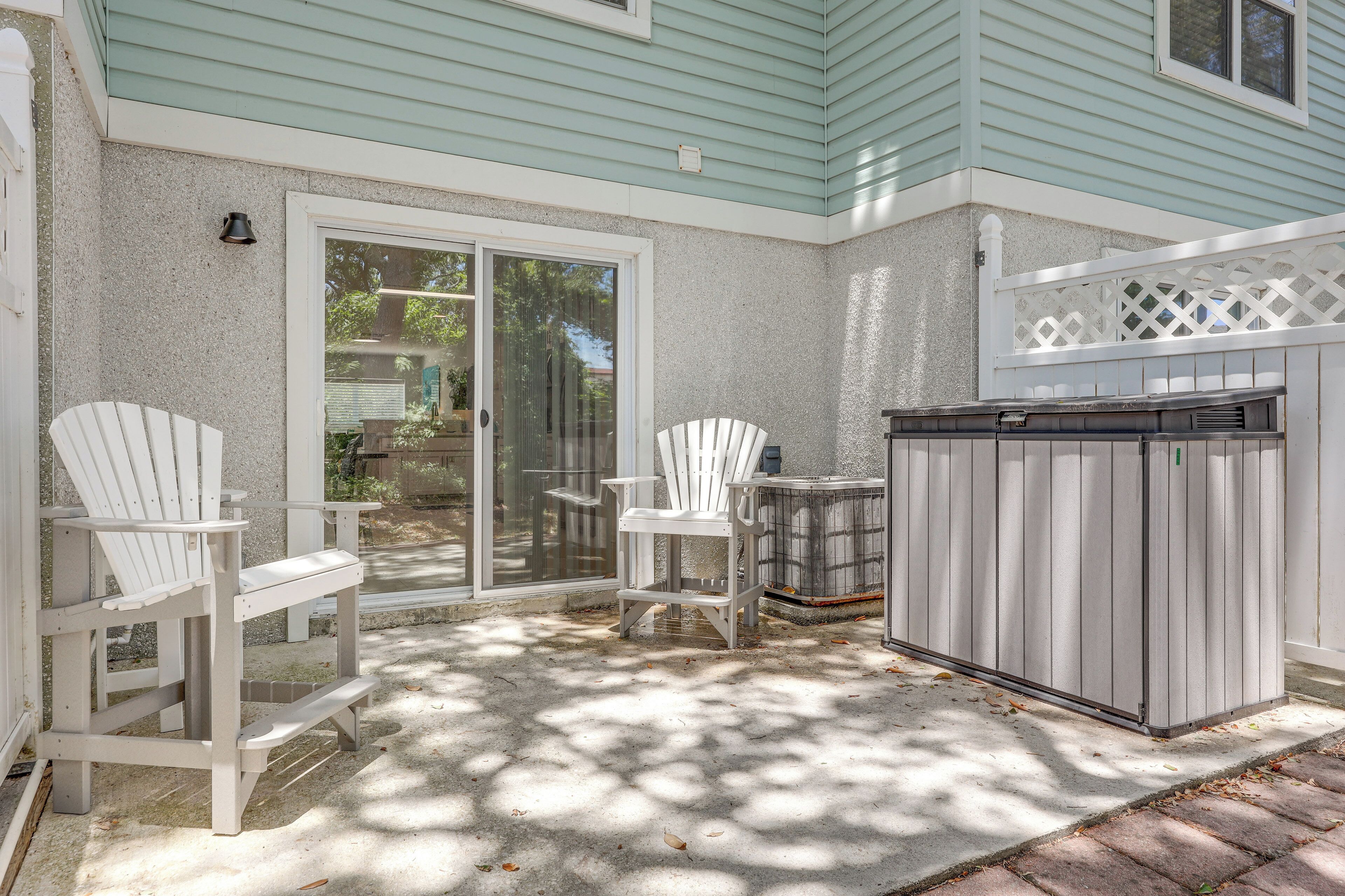 A covered patio area with two Adirondack chairs, a grill, and a sliding glass door leading to a backyard.