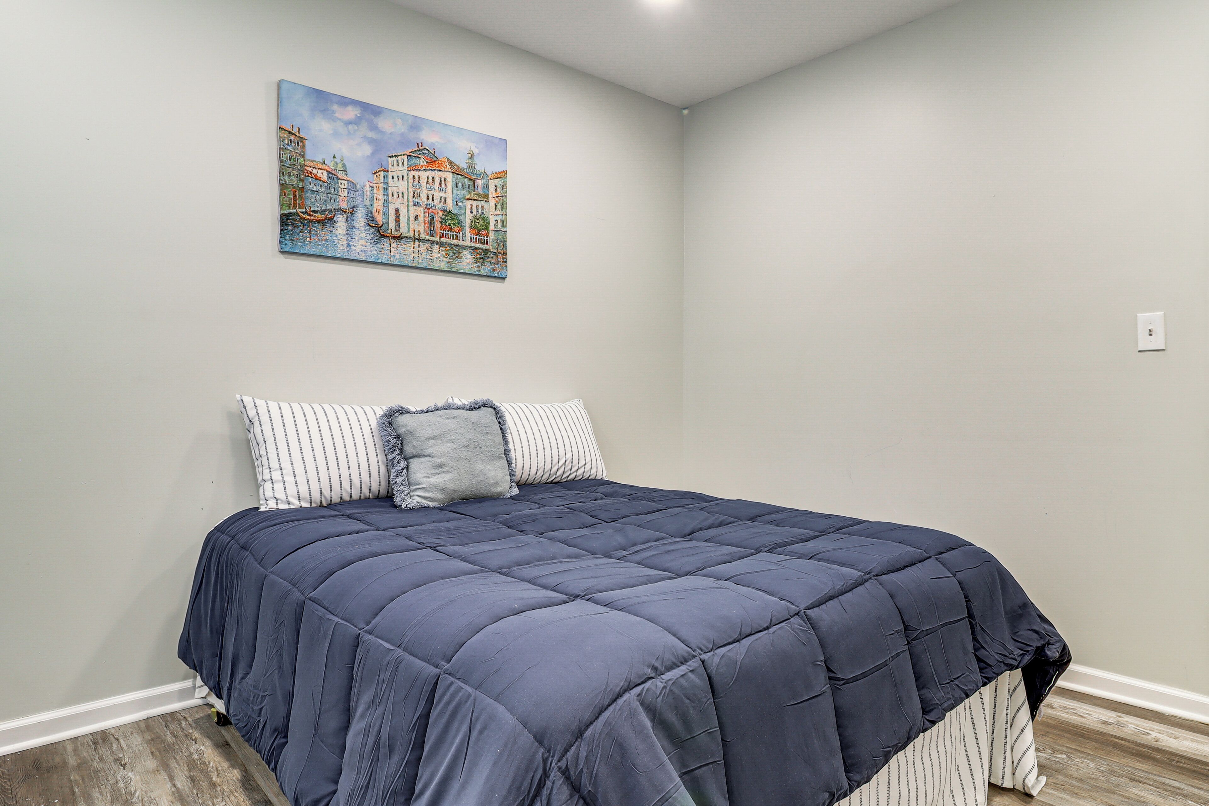 Ein Schlafzimmer mit einem Bett, einem Gemälde einer Kanalansicht und einem Lichtschalter an der Wand.