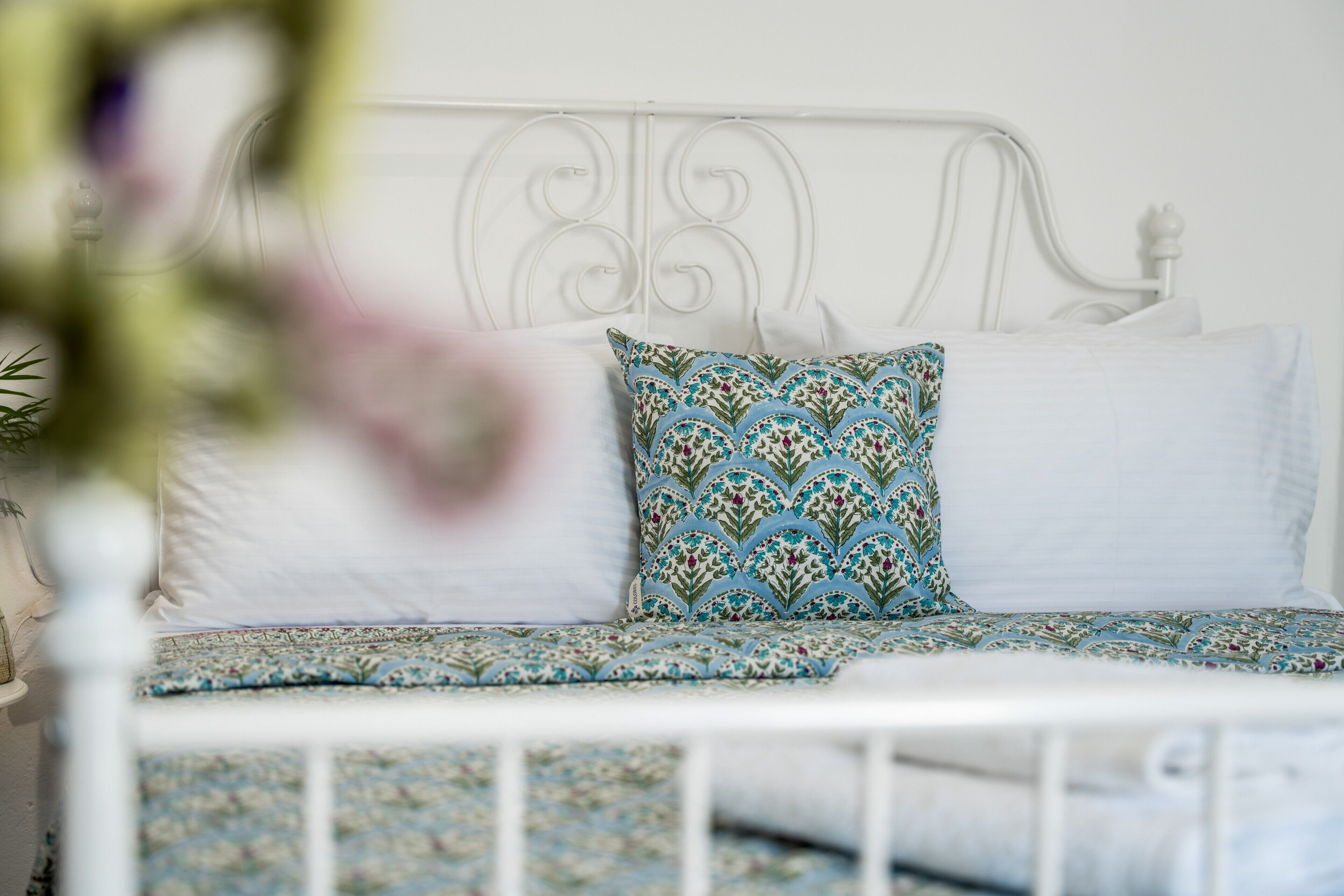 A white metal bed frame with a patterned bedspread and pillows.