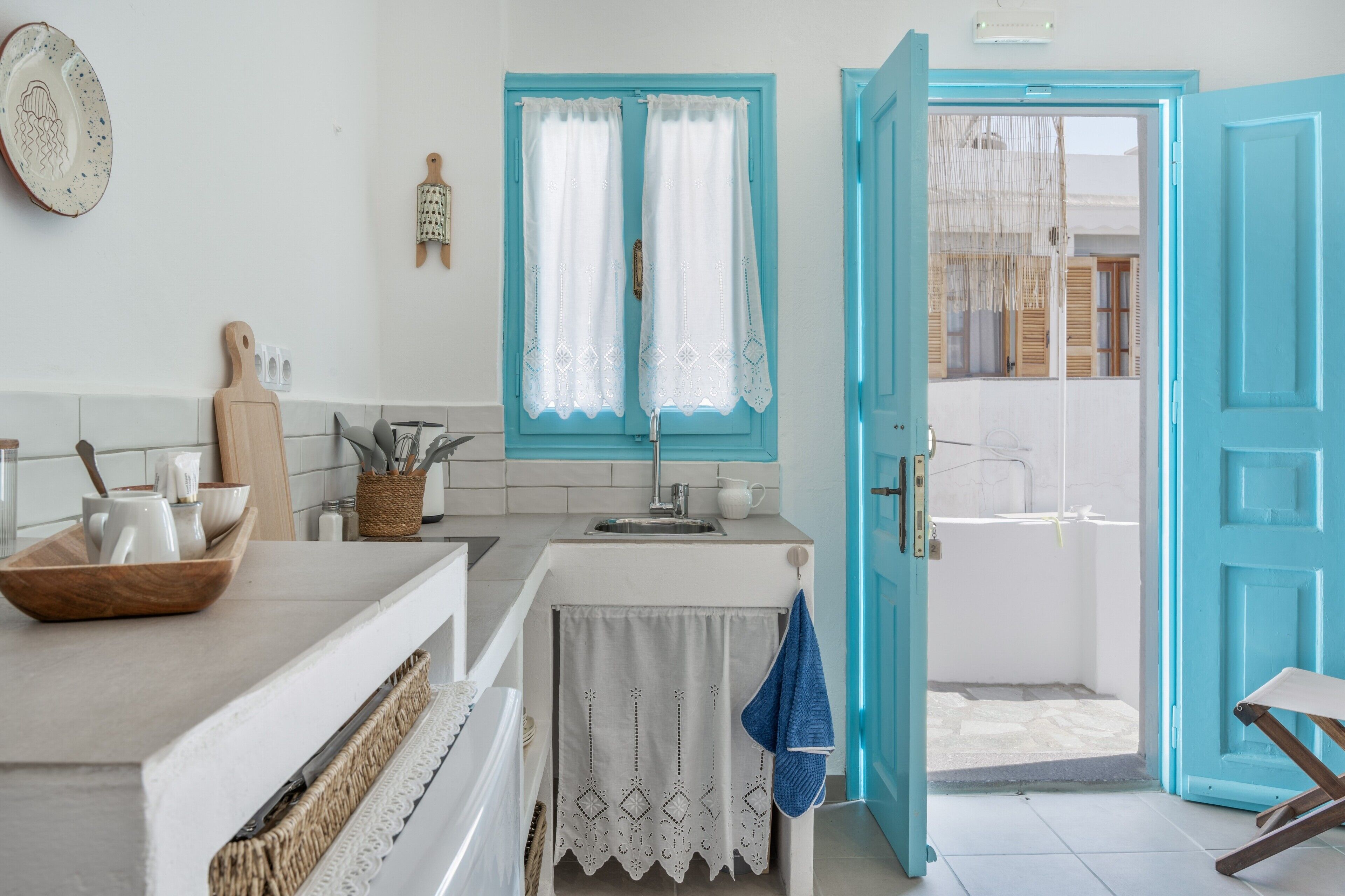 A kitchen with a sink, a cutting board, and a window with curtains.