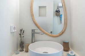 Un baño con un lavamanos blanco, un espejo con marco de madera, una ventana pequeña y un perchero para toallas.