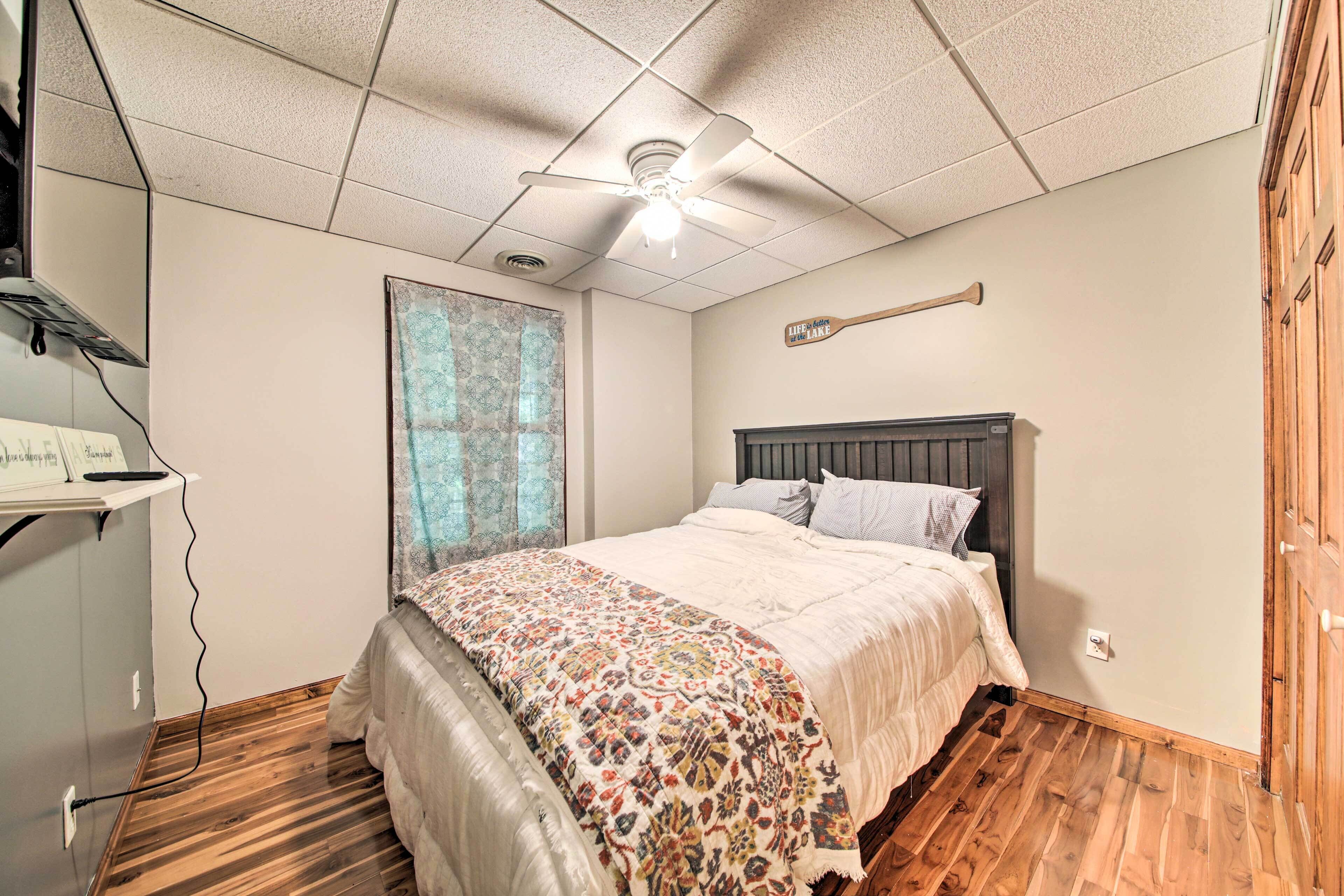 Un dormitorio con cama, ventilador de techo, ventana con cortinas y piso de madera.