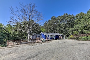 A small, single-story building with a blue exterior and a sloped roof, surrounded by a gravel driveway and a wooden fence. - Lake Shelbyville Retreat! Cabin 1 Mi to Water (Shelbyville)