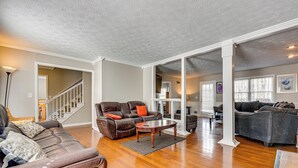 A spacious living room with a brown leather sofa, a wooden coffee table, and a staircase leading to another level. - Centrally Located Fayetteville Home: Deck + Yard (Fayetteville)