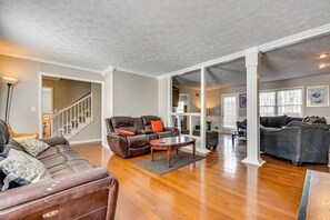 A spacious living room with a brown leather sofa, a wooden coffee table, and a staircase leading to another level. - Centrally Located Fayetteville Home: Deck + Yard (Fayetteville)