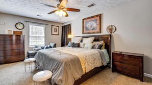 A bedroom with a bed, a dresser, a vanity, a ceiling fan, and a window. - Centrally Located Fayetteville Home: Deck + Yard (Fayetteville)