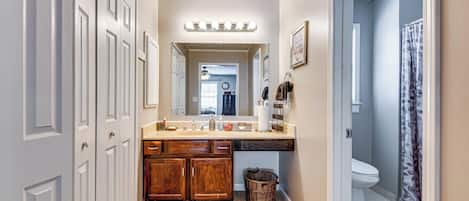 A hallway with a bathroom, a vanity with a mirror, and a shower curtain.