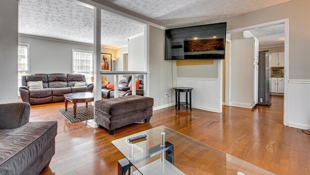 A spacious living room with a large TV, leather sofas, and hardwood floors. - Centrally Located Fayetteville Home: Deck + Yard (Fayetteville)