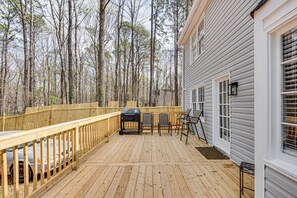 Un patio in legno con barbecue, sedie e tavolo.