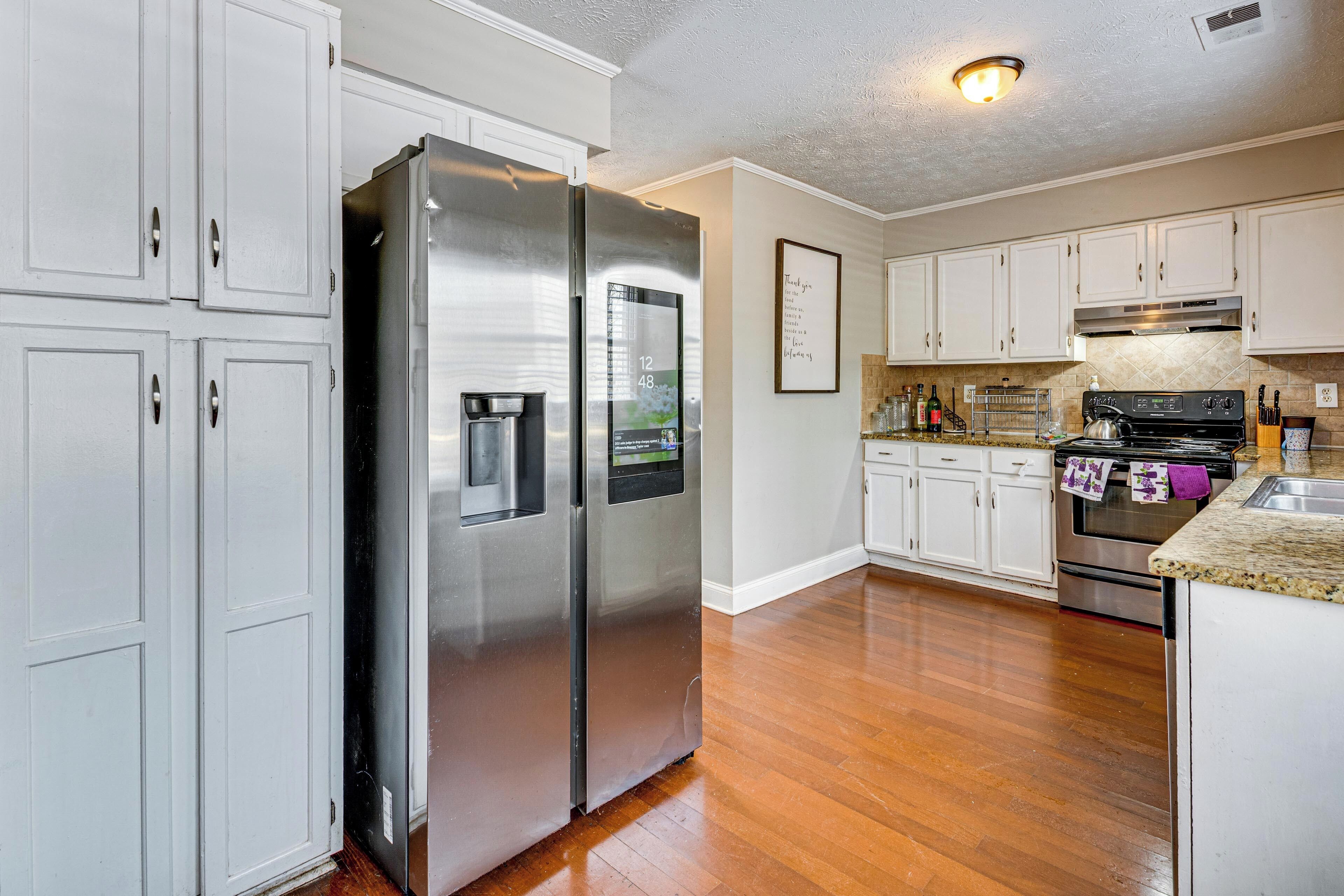 A kitchen with white cabinets, stainless steel appliances, and a wooden floor.