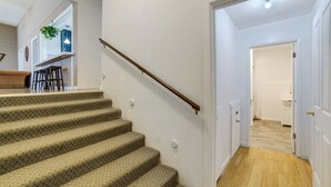 Portaat, joiden askelmat on päällystetty matolla, johtavat ylätasanteelle. Lattia on tehty puusta, ja portaikon päässä on valkoinen ovi.