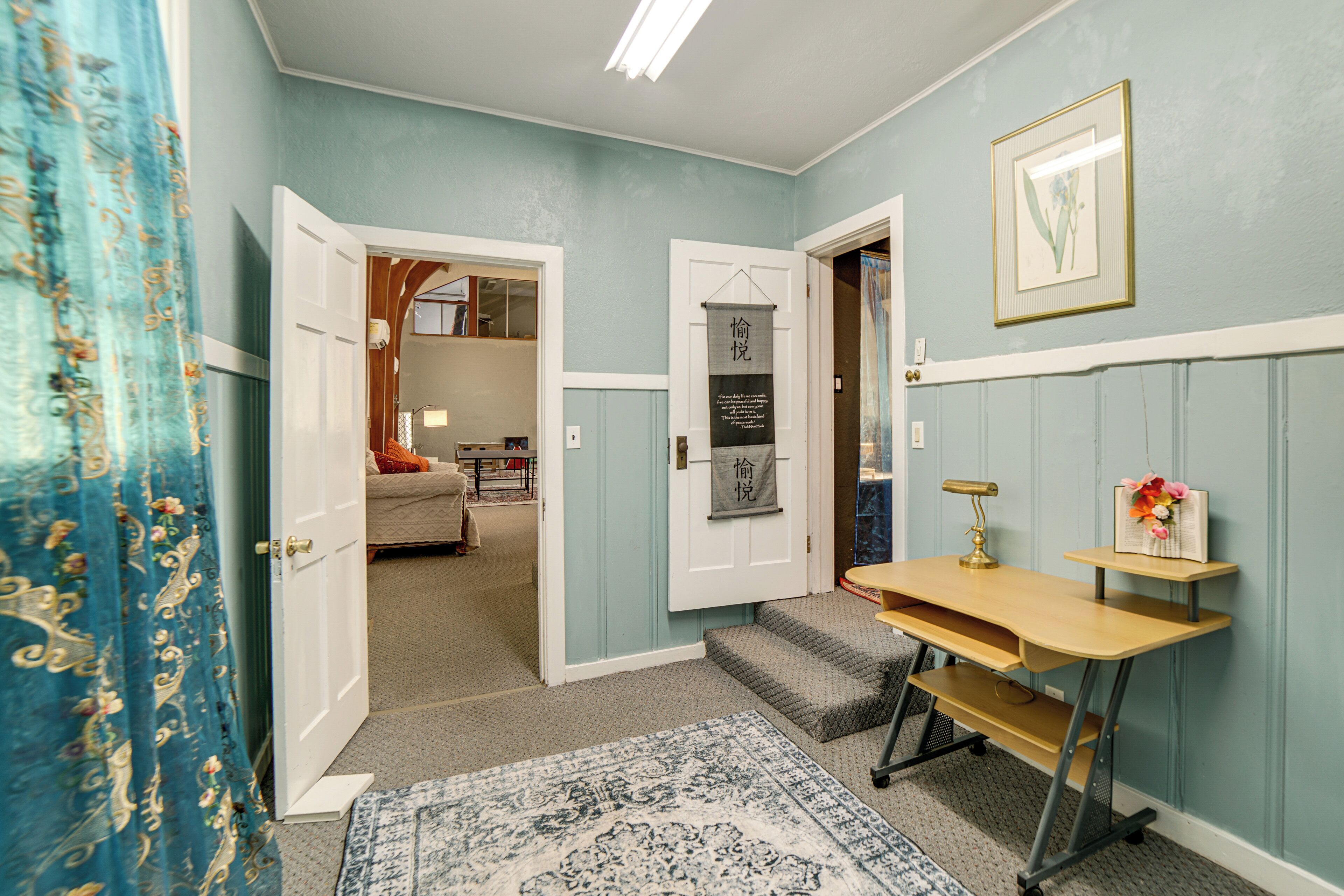 A hallway with a patterned rug, a desk with a lamp, and a door leading to a bedroom.