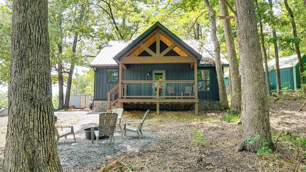 Eine Hütte mit Veranda, umgeben von Bäumen und Sitzgelegenheiten im Freien.