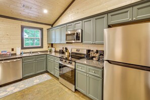 A modern kitchen with stainless steel appliances, green cabinets, and a window with a view of trees. - Walk to Water: Irvin Cobb Resort Cabin! (Murray)
