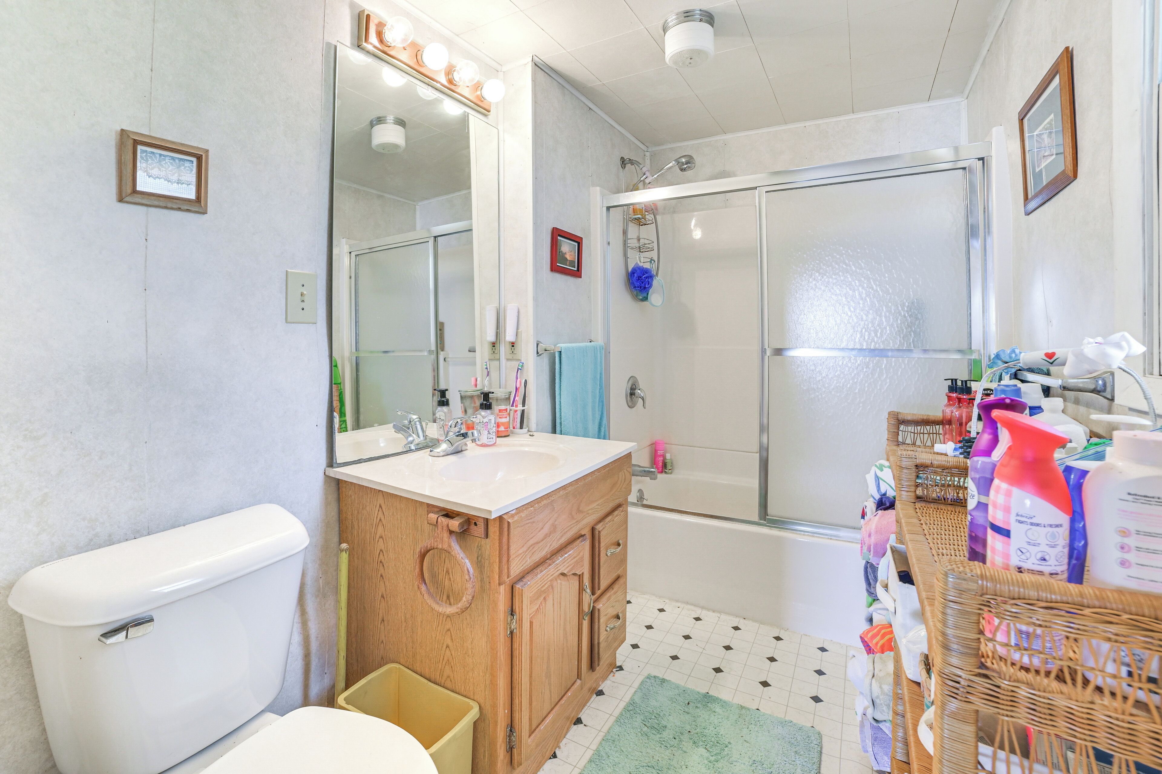 A bathroom with a toilet, sink, mirror, shower, and various toiletries.