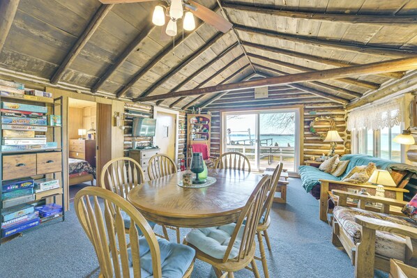A log cabin interior with a dining area, wooden furniture, and a view through a large window.
