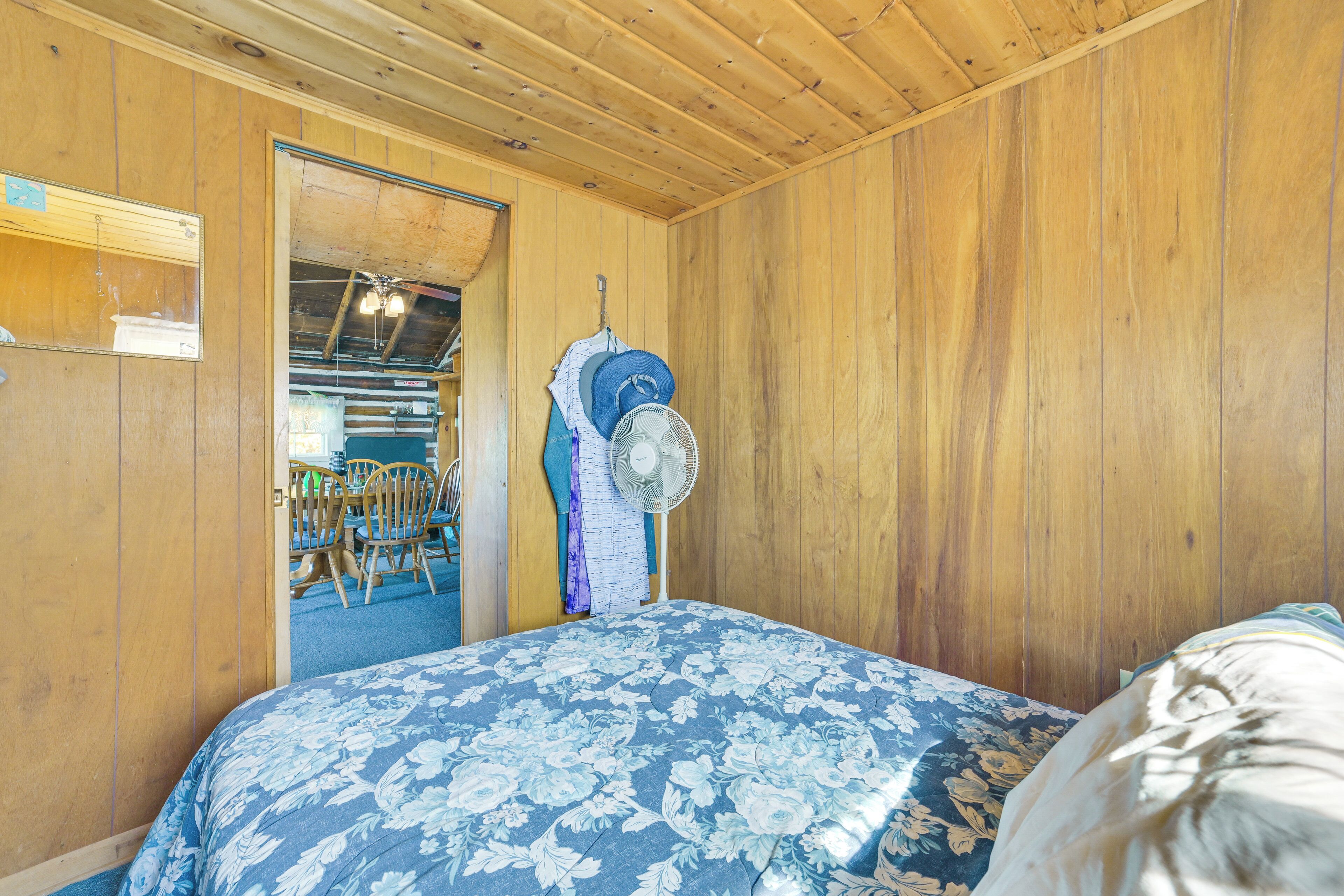 Una habitación con paneles de madera, una cama, un ventilador y una puerta que da a un comedor.