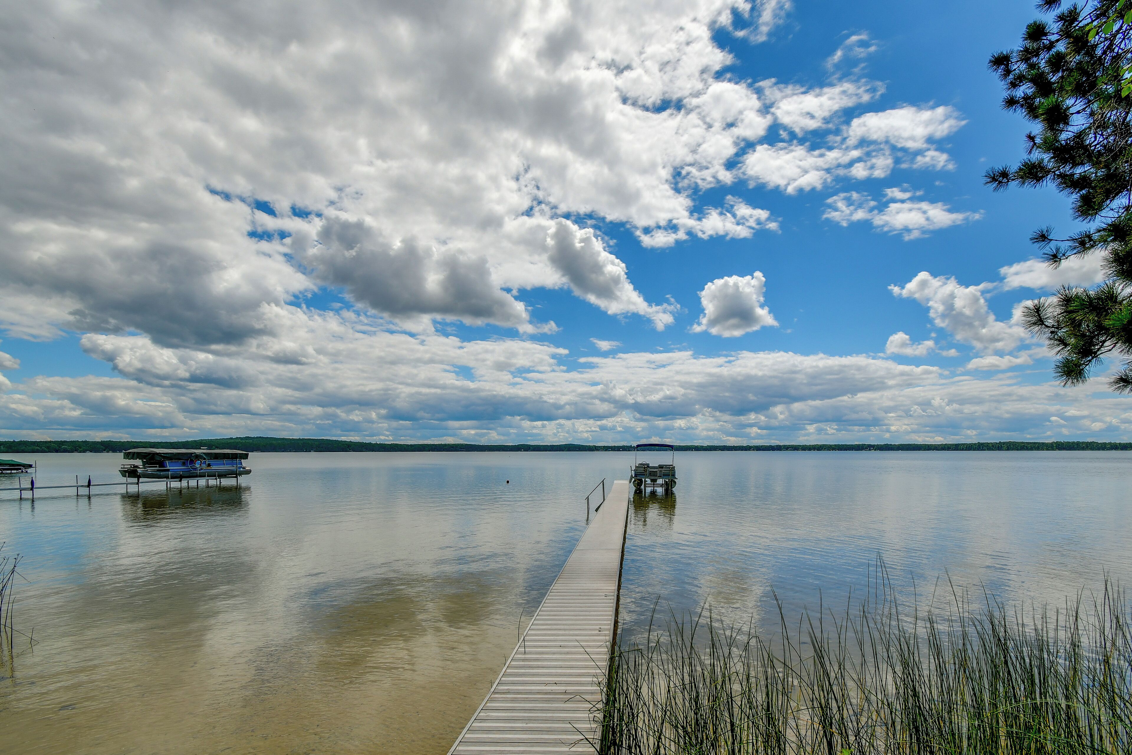 Un lac paisible avec une jetée en bois qui s’avance sur l’eau, entouré d’arbres et surplombé d’un ciel partiellement nuageux.