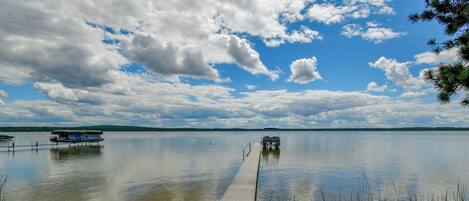 A calm lake with a wooden dock extending into the water, surrounded by trees and a partly cloudy sky.