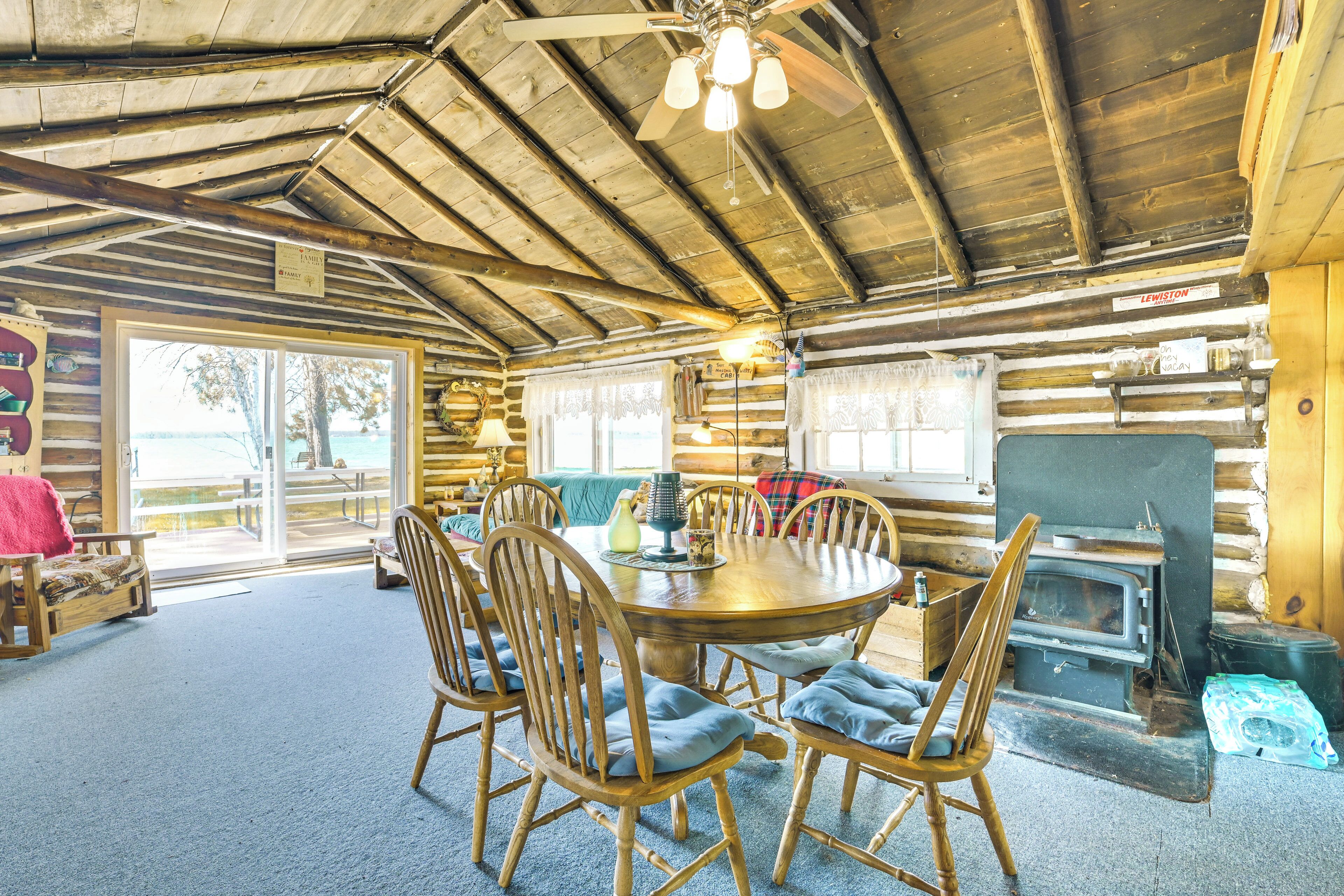 L’intérieur d’une cabane en rondins, avec une table de salle à manger ronde en bois entourée de chaises, une cheminée et un ventilateur de plafond.
