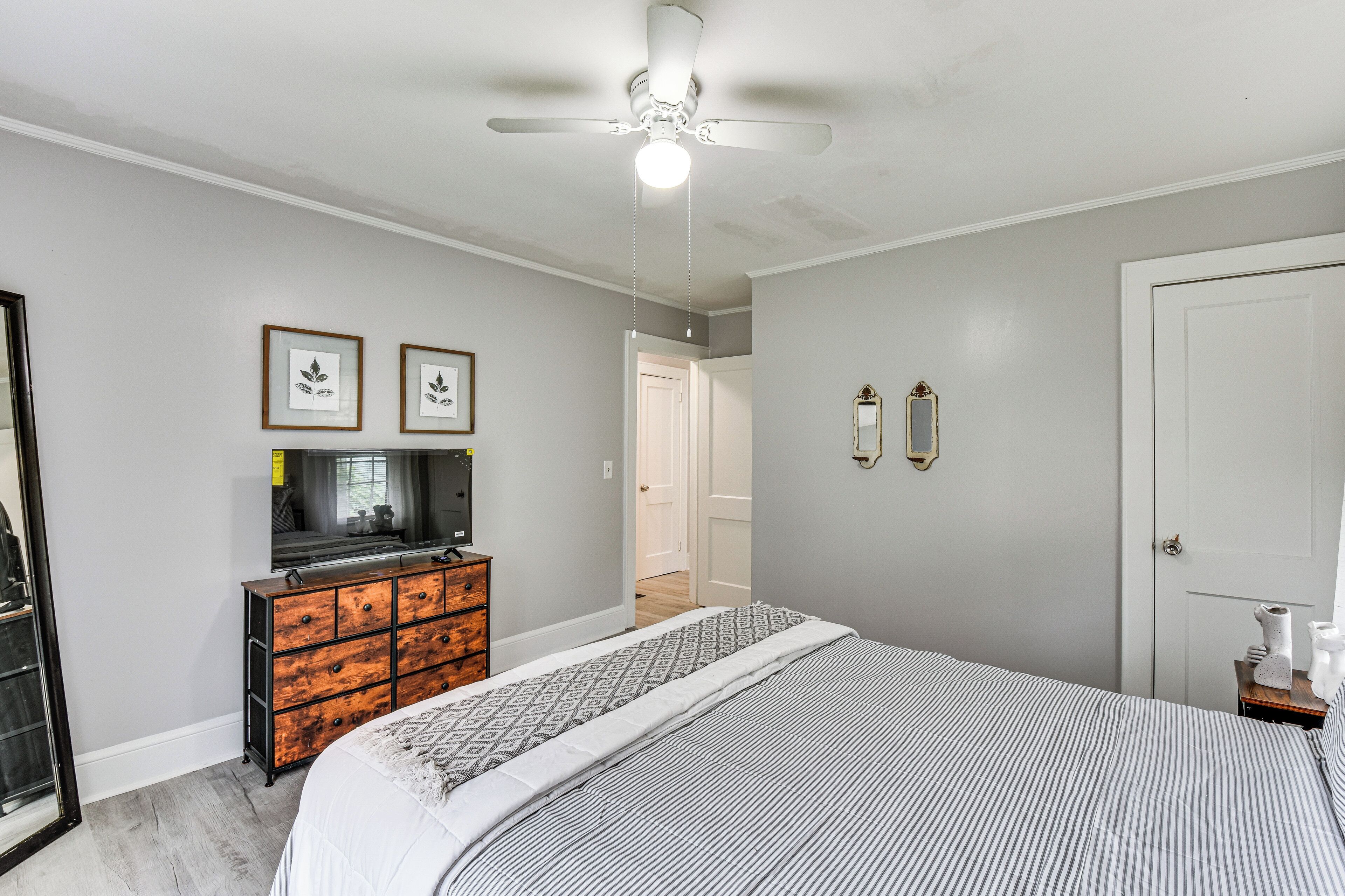 Une chambre à coucher avec un lit, une commode, un ventilateur de plafond et des tableaux encadrés accrochés au mur.