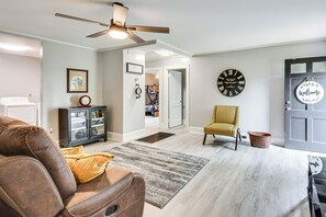 A living room with a brown leather sofa, a yellow armchair, a black clock, and a door with a 'Welcome' sign. - Walkable Location! Peaceful Toccoa Escape w/ Yard (Toccoa)
