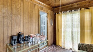 A wooden-paneled room with a glass coffee table, a bed with patterned bedding, and a window with yellow curtains. - Walkable Location! Peaceful Toccoa Escape w/ Yard (Toccoa)