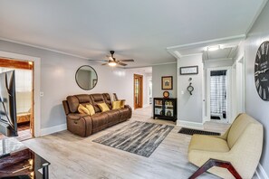 A living room with a brown leather sofa, a beige armchair, a ceiling fan, and a wooden floor. - Walkable Location! Peaceful Toccoa Escape w/ Yard (Toccoa)