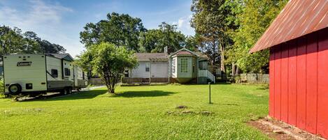 A green trailer, a small house, and a red barn in a grassy yard.