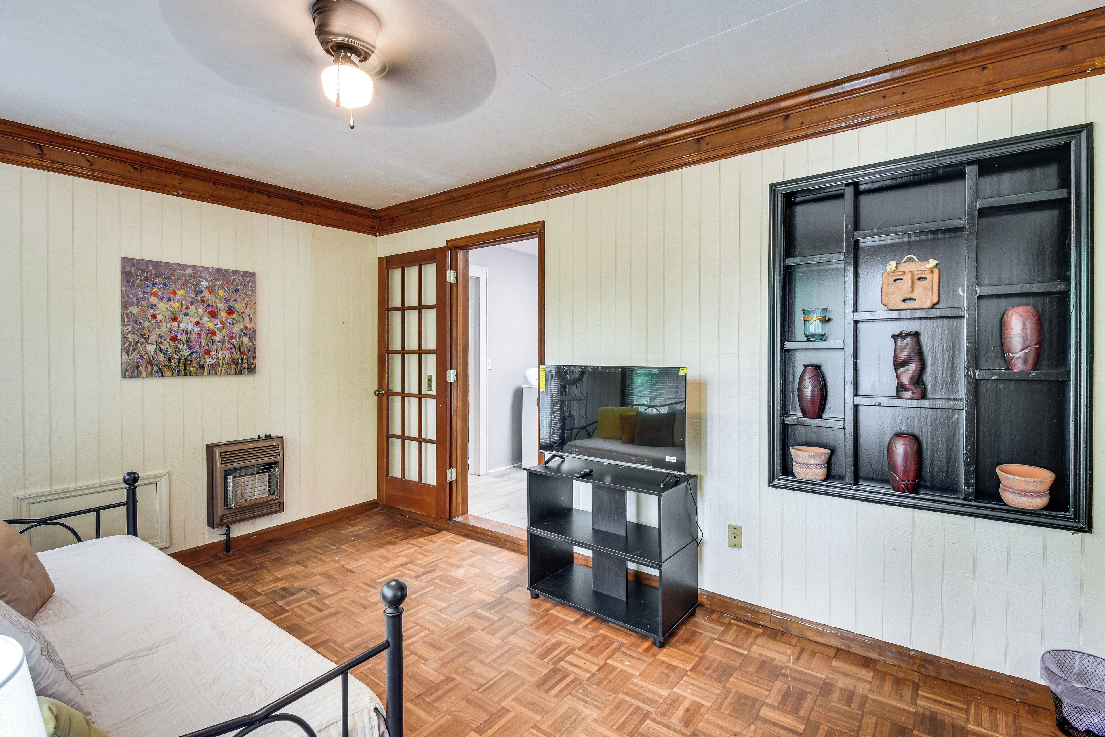 A room with a bed, a television, a fireplace, a door, and a wall display.