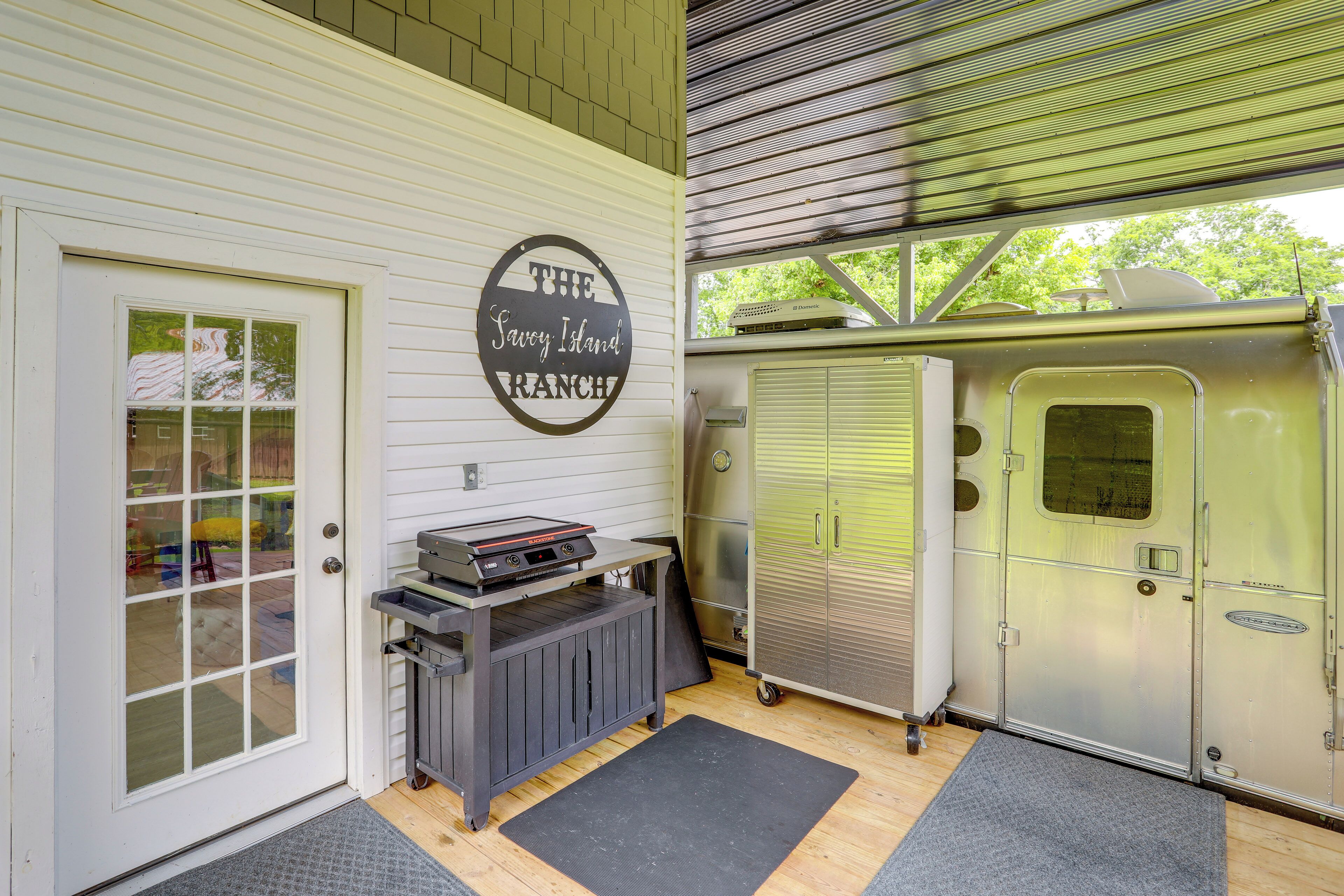 A covered outdoor area with a metal trailer, a metal cabinet, and a door with a window.