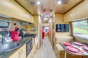 A compact kitchen with a sink, stove, and coffee maker, a dining area with plates, and a TV. - 2-studio Retreat on White River w/ Swimming Hole (Mountain View)