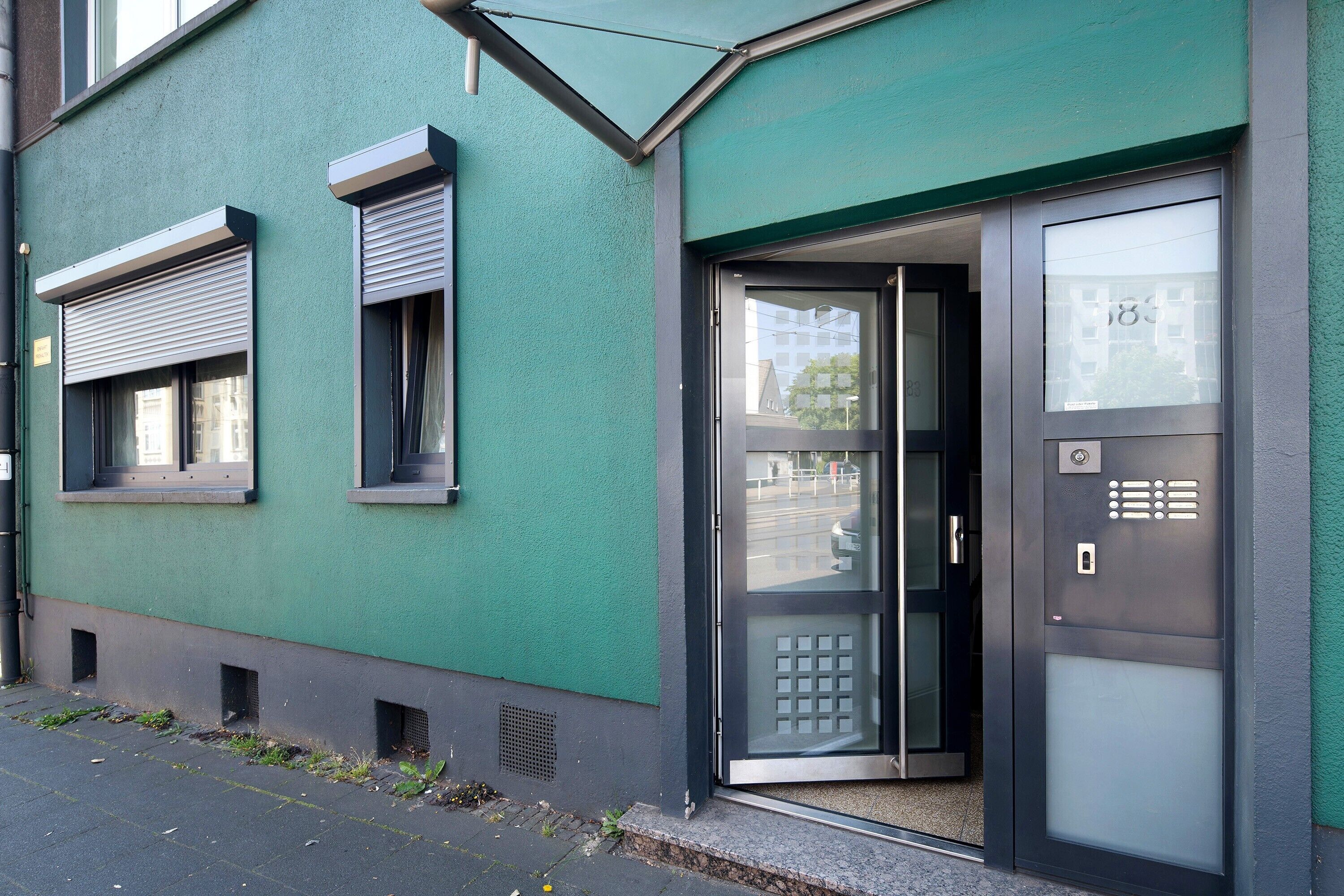 Ein Gebäude mit grüner Fassade, einer Tür mit satiniertem Glas und einem Fenster mit Rollo.