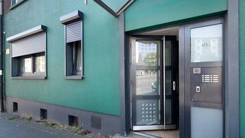 Ein Gebäude mit grüner Fassade, einer Tür mit satiniertem Glas und einem Fenster mit Rollo.