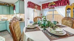 Uma área de refeições com uma mesa posta para quatro pessoas, cadeiras e uma janela com cortinas.