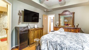 Quarto com cama, televisão, cómoda de madeira, espelho e um pequeno frigorífico.