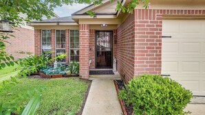 Uma casa residencial com fachada de tijolos, porta principal, porta de garagem e um pequeno jardim frontal com plantas.
