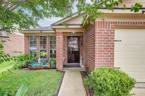 A residential house with a brick exterior, a front door, a garage door, and a small front yard with plants. - 4 Mi to Lake Houston! Single-level Home w/ Yard (Humble)