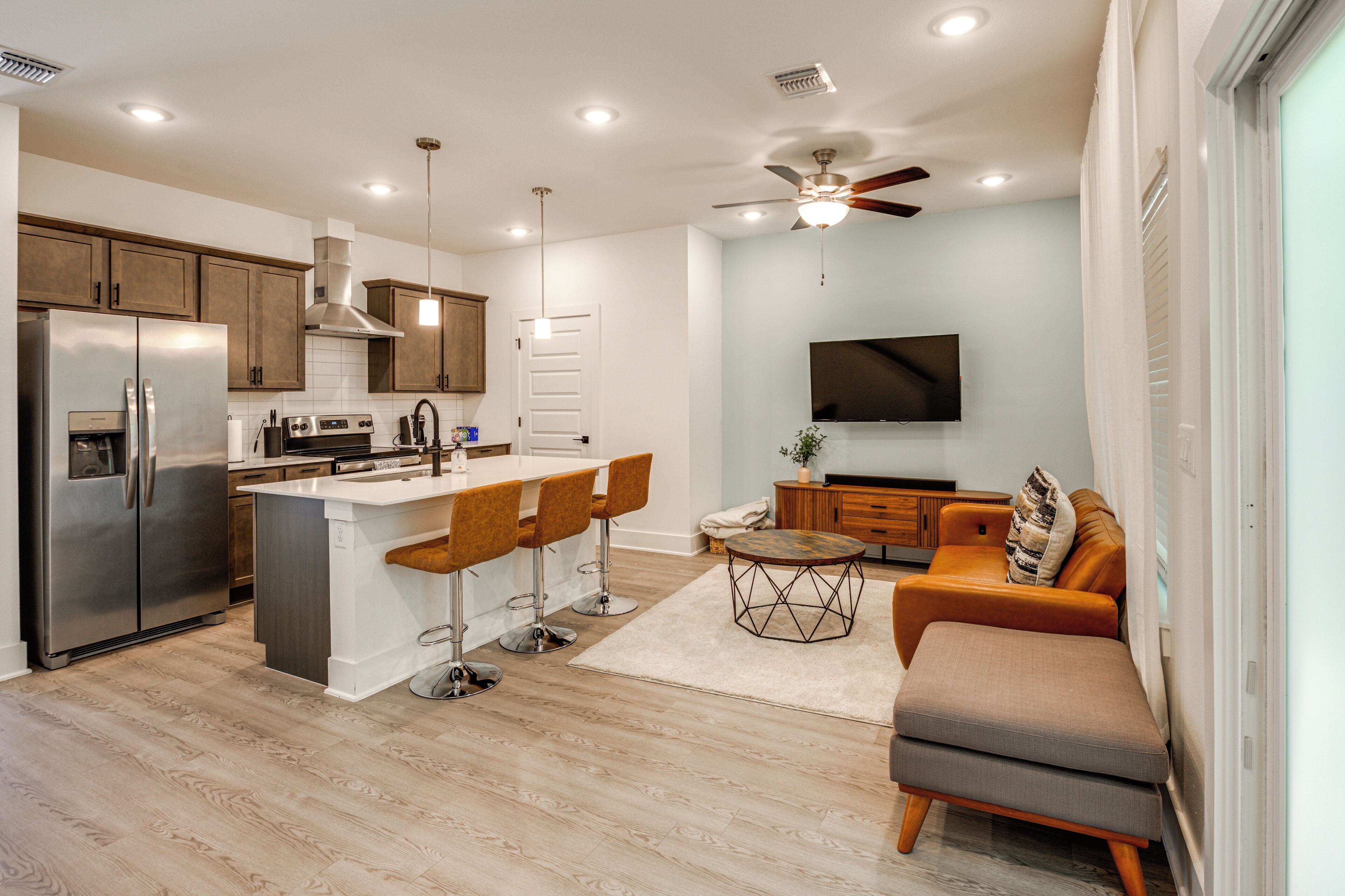 A modern kitchen with a central island, bar stools, a dining table, and a ceiling fan.